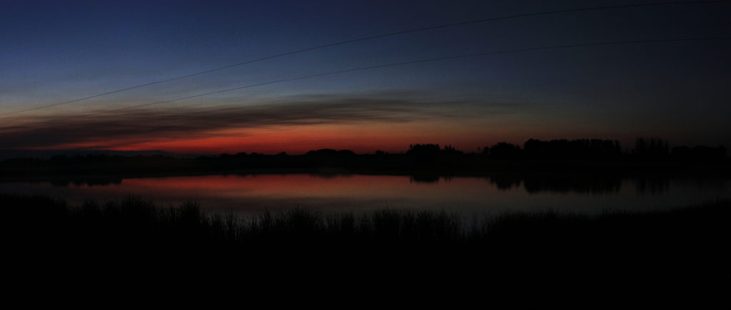 Panorama: post-sunset glow (red and orange below, dark blue above) reflected in a pond