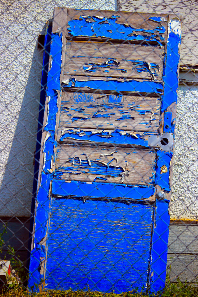 A bright blue door leans against a building.