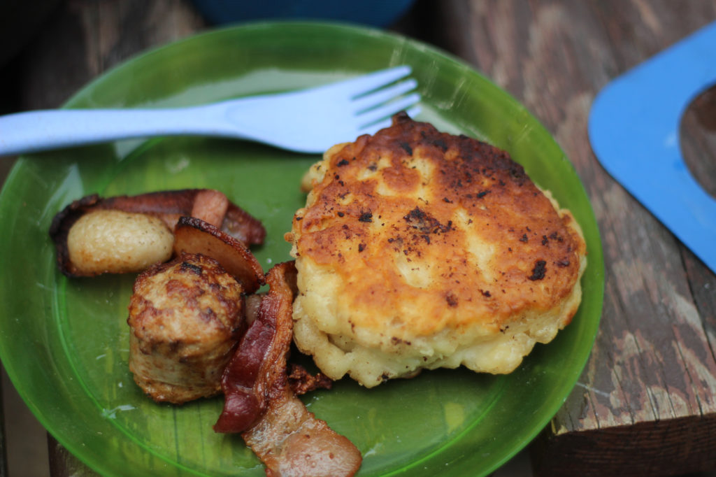 A green plate with bacon, Italian sausage, and bannock on it