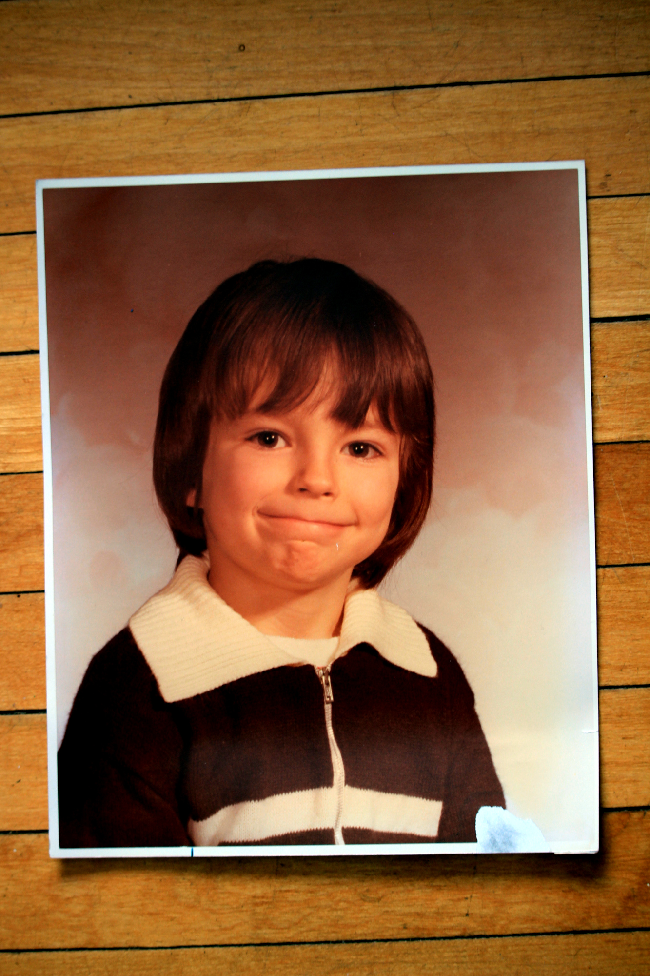 A photo of me in kindergarten, back in the late 1900s; I'm wearing a brown-and-beige zip-up sweatshirt and I've got a sort of smile, lips tightly shut